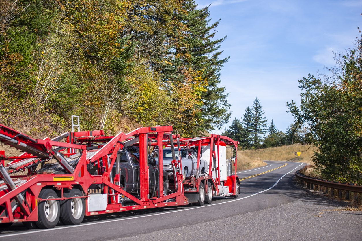 Loaded car hauler on a wooded highway in autumn