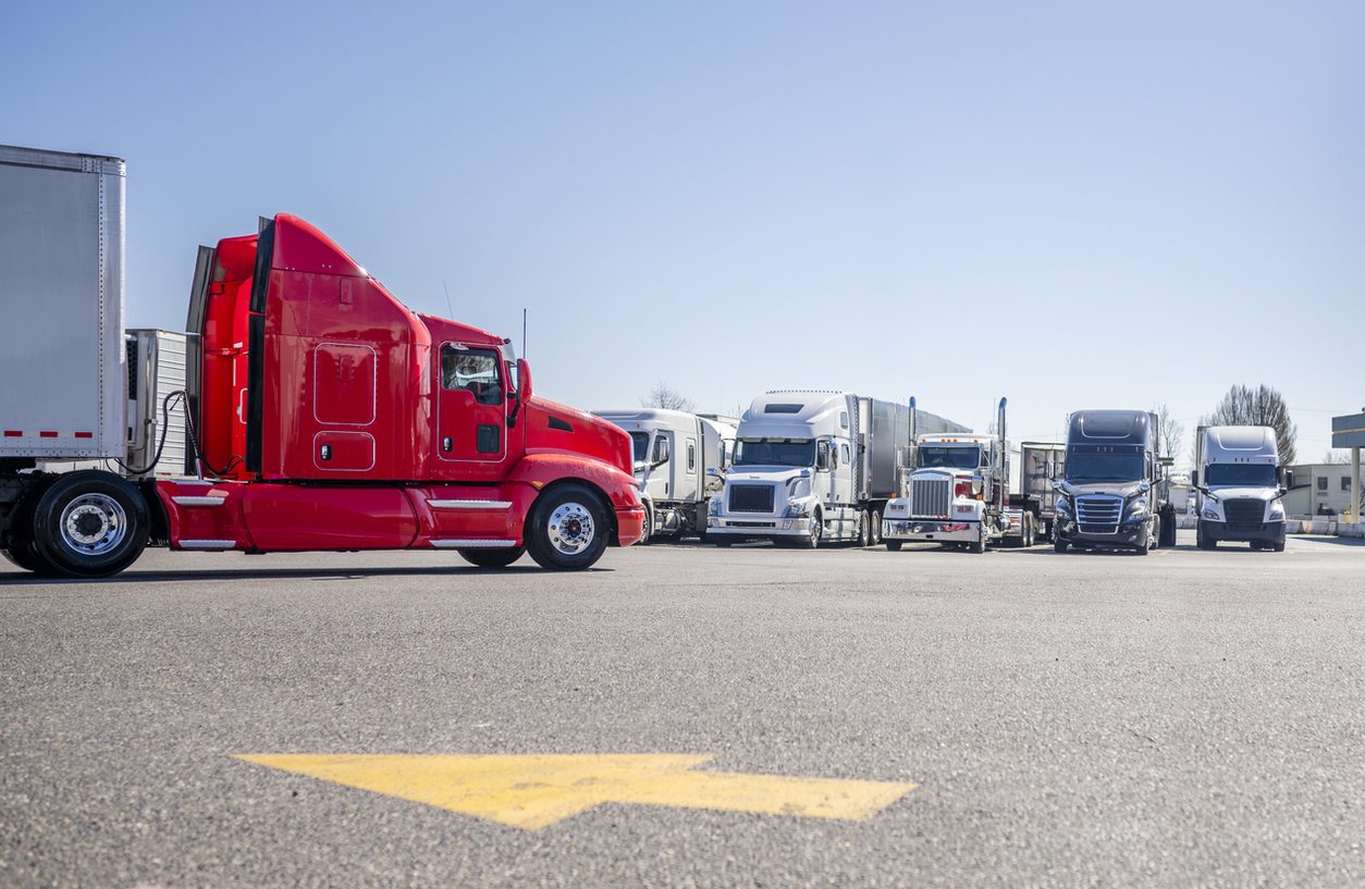 Red semi truck moving through a truck stop parking lot