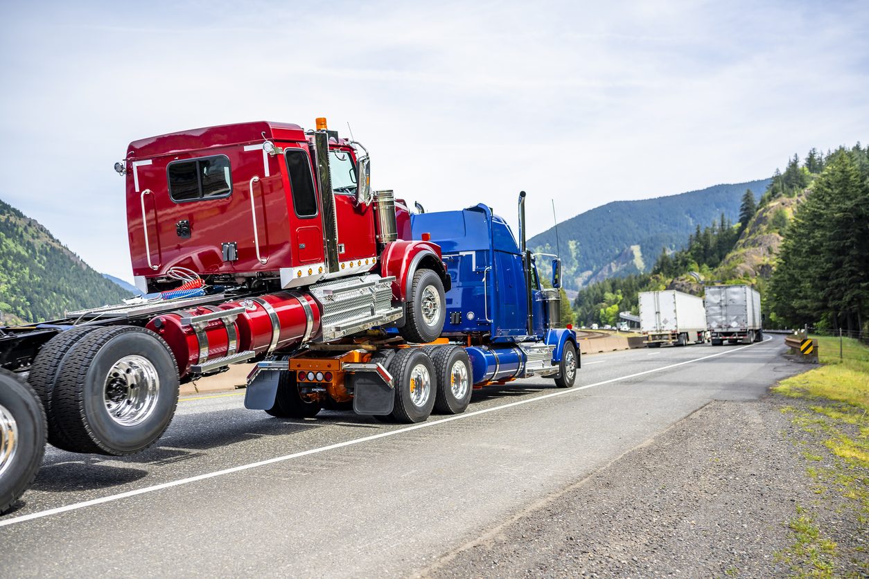 Conventional tractor hauling equipment on a highway through hills