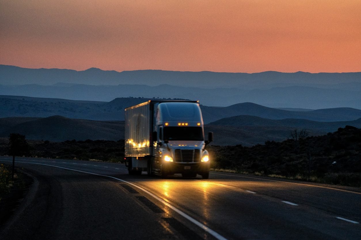 Conventional tractor with headlights on a desert highway at dusk