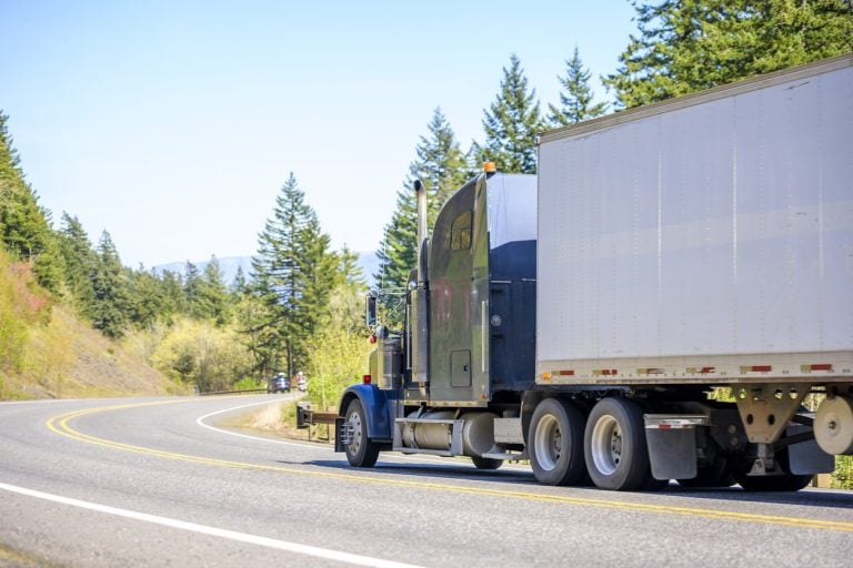 Highway tractor and trailer on a road through forest
