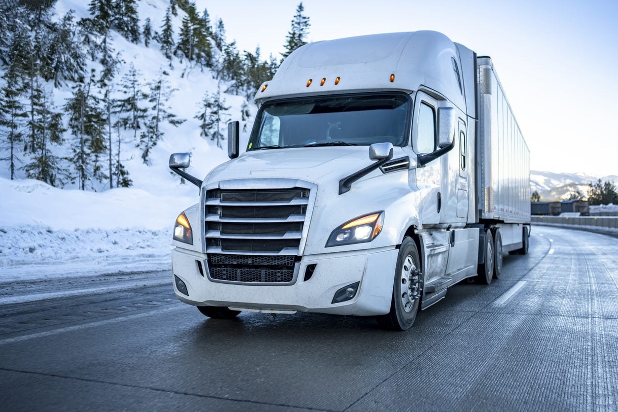 Semi truck running a snow covered highway with headlights on