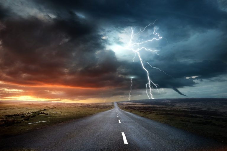 Lightning striking beyond an empty road under storm cloud