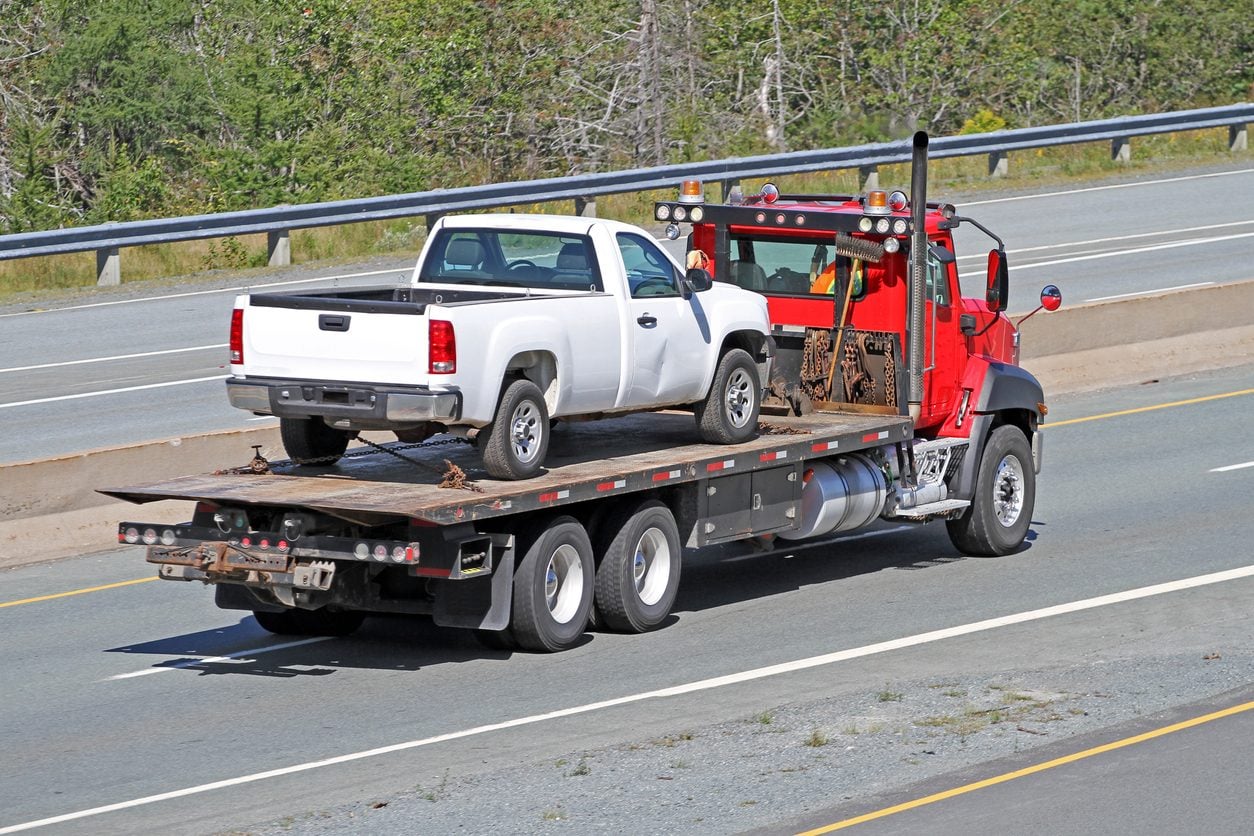 Tilt bed tow truck carrying a pickup on a highway