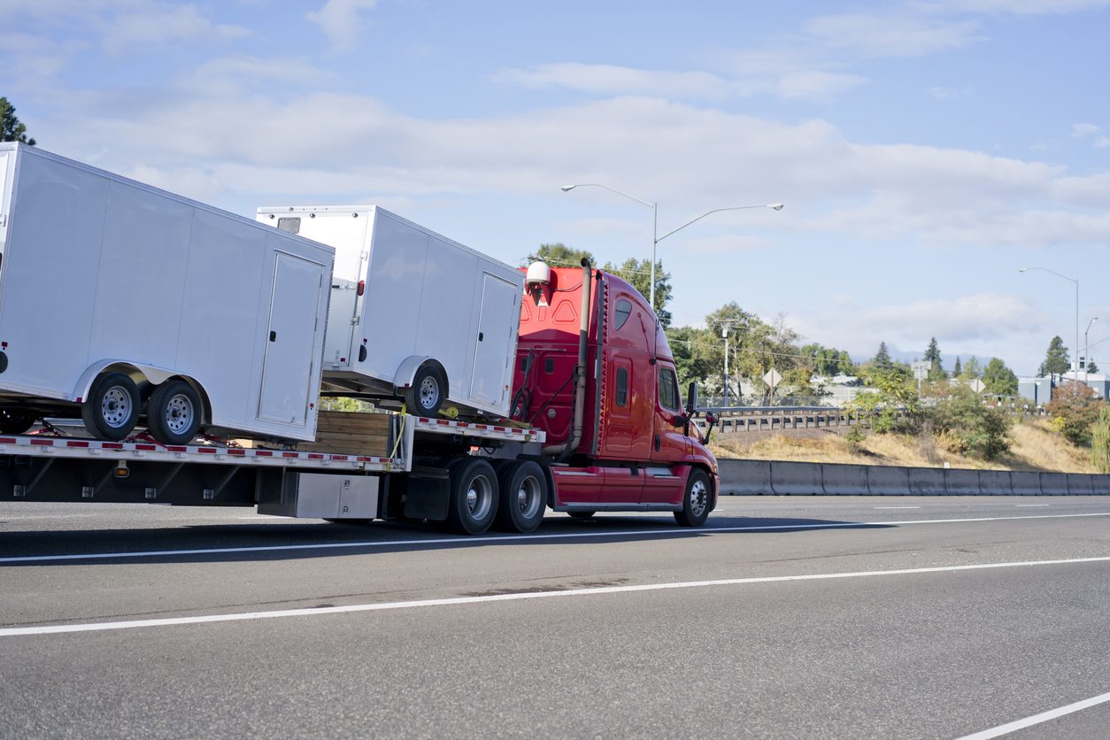 Red conventional tractor hauling trailers on a step deck