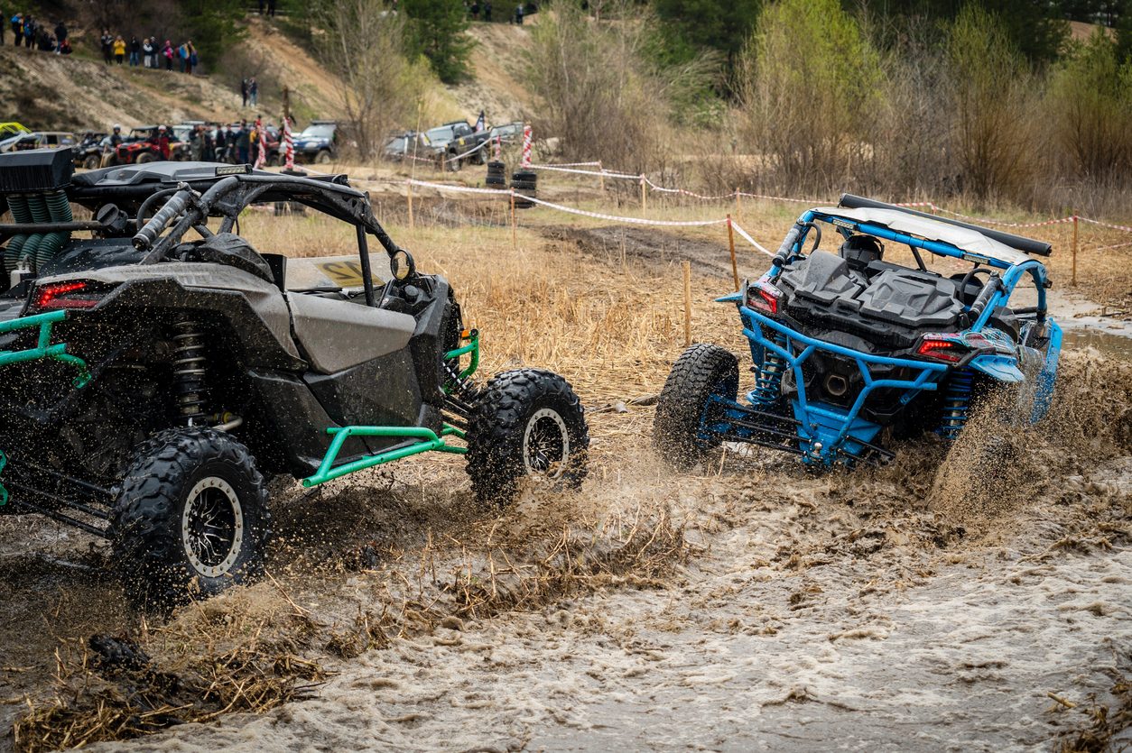 Side by side UTVs racing through mud and water