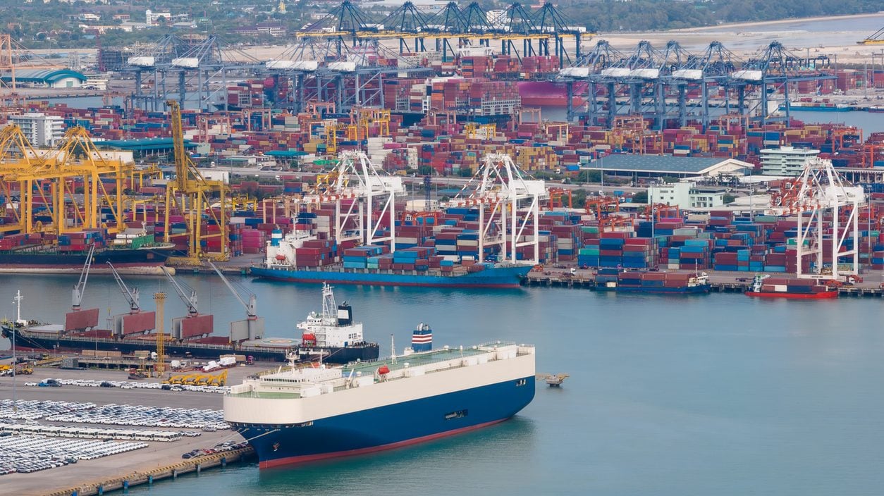 Vehicle carrier berthed at a port with new cars waiting on the quay