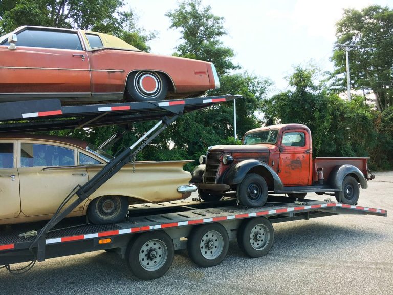 Vintage American cars and an early pickup loaded on an open trailer