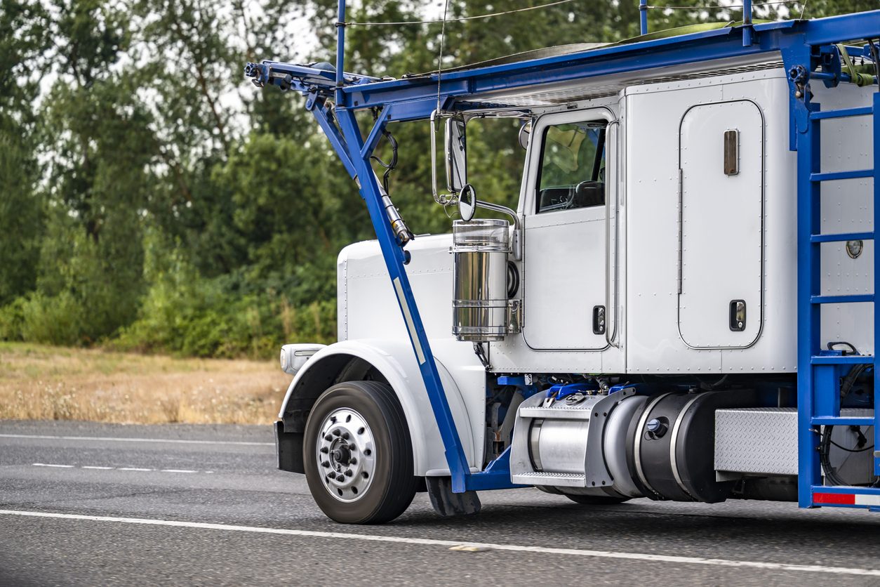 White car hauler tractor running a tree lined road