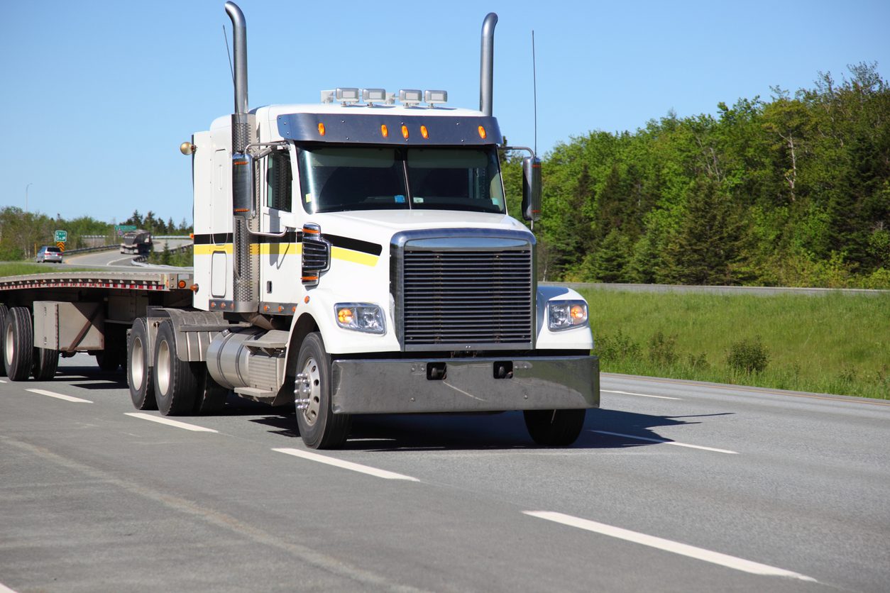 White conventional tractor with a flatbed trailer on a highway