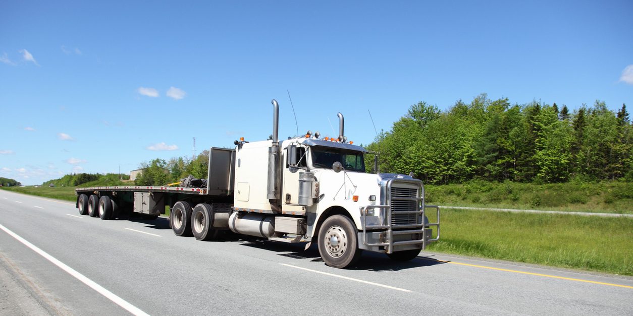 White conventional tractor and trailer on a rural highway