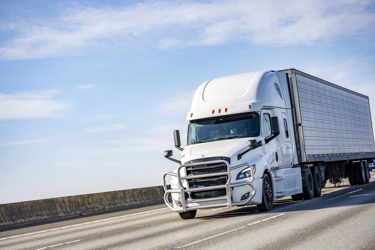 White conventional tractor with a refrigerated trailer on a highway