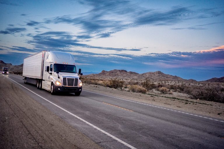 White conventional tractor with a trailer on a desert highway at dusk