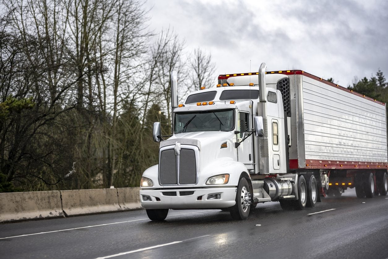 Highway tractor and trailer traveling a wet road through wooded country