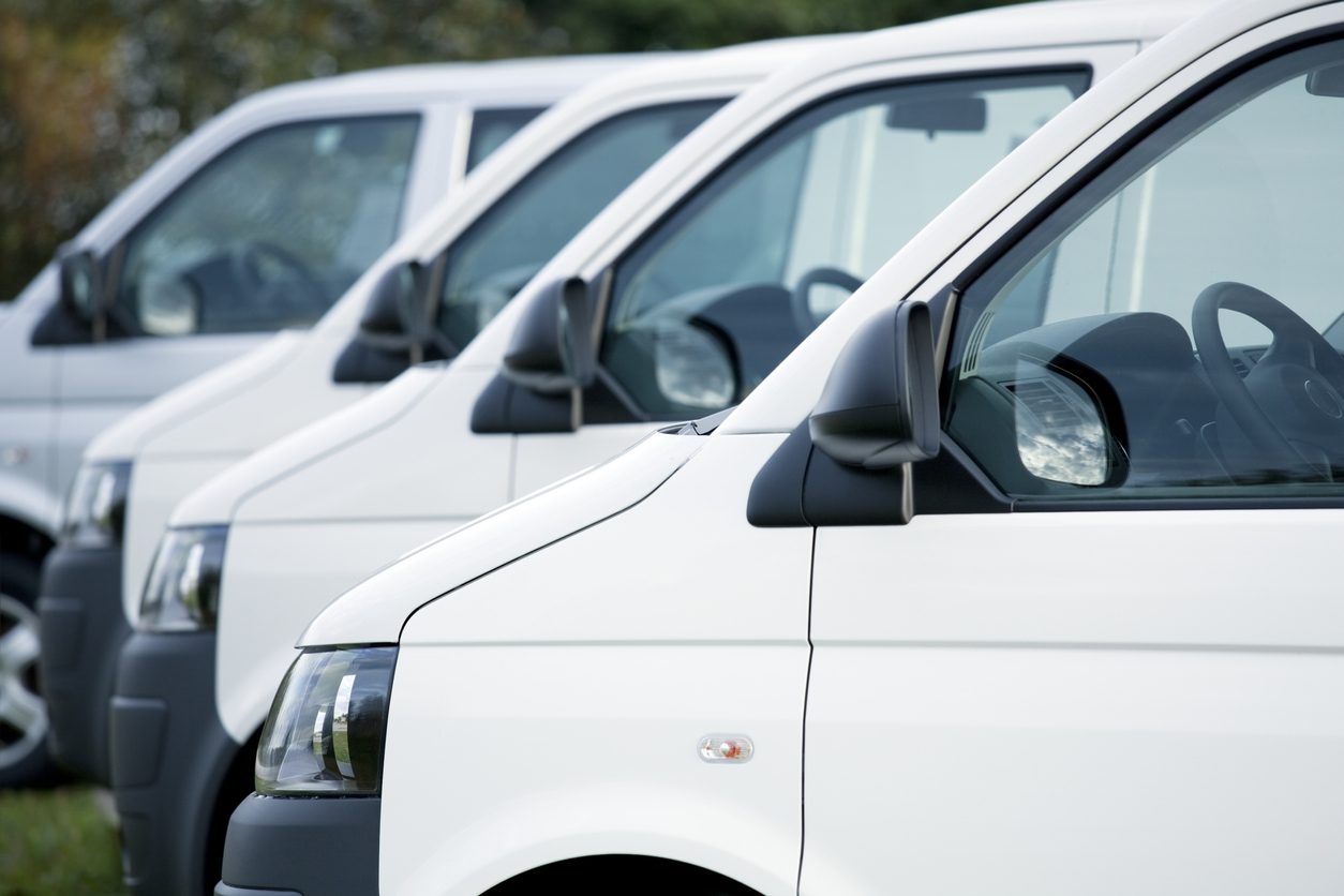 Row of white cargo vans at a depot