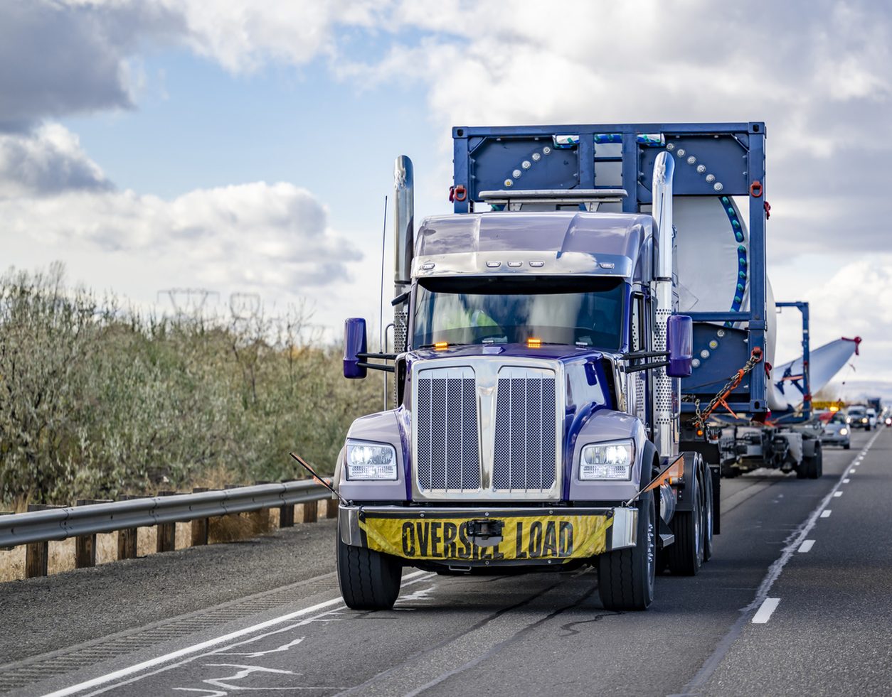 Tractor hauling a wind turbine blade with an escort vehicle