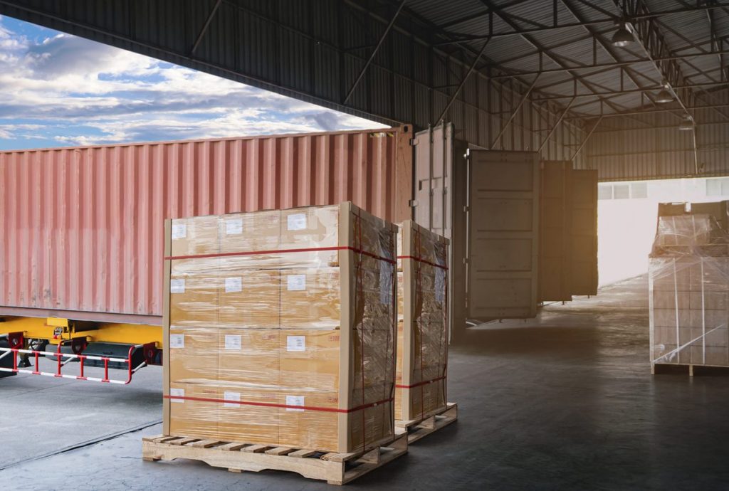 Stretch wrapped pallet of boxes beside a container at a dock