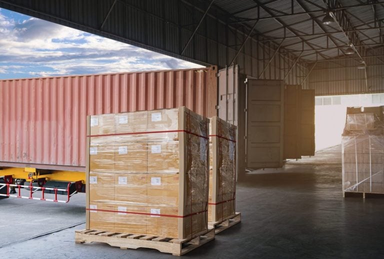 Stretch wrapped pallet of boxes beside a container at a dock