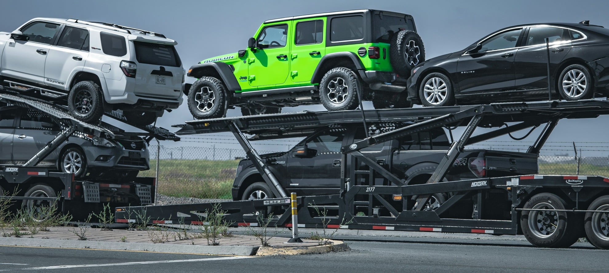 Two deck car carrier fully loaded with a white SUV, a bright green Jeep, a black sedan and more vehicles on the lower deck