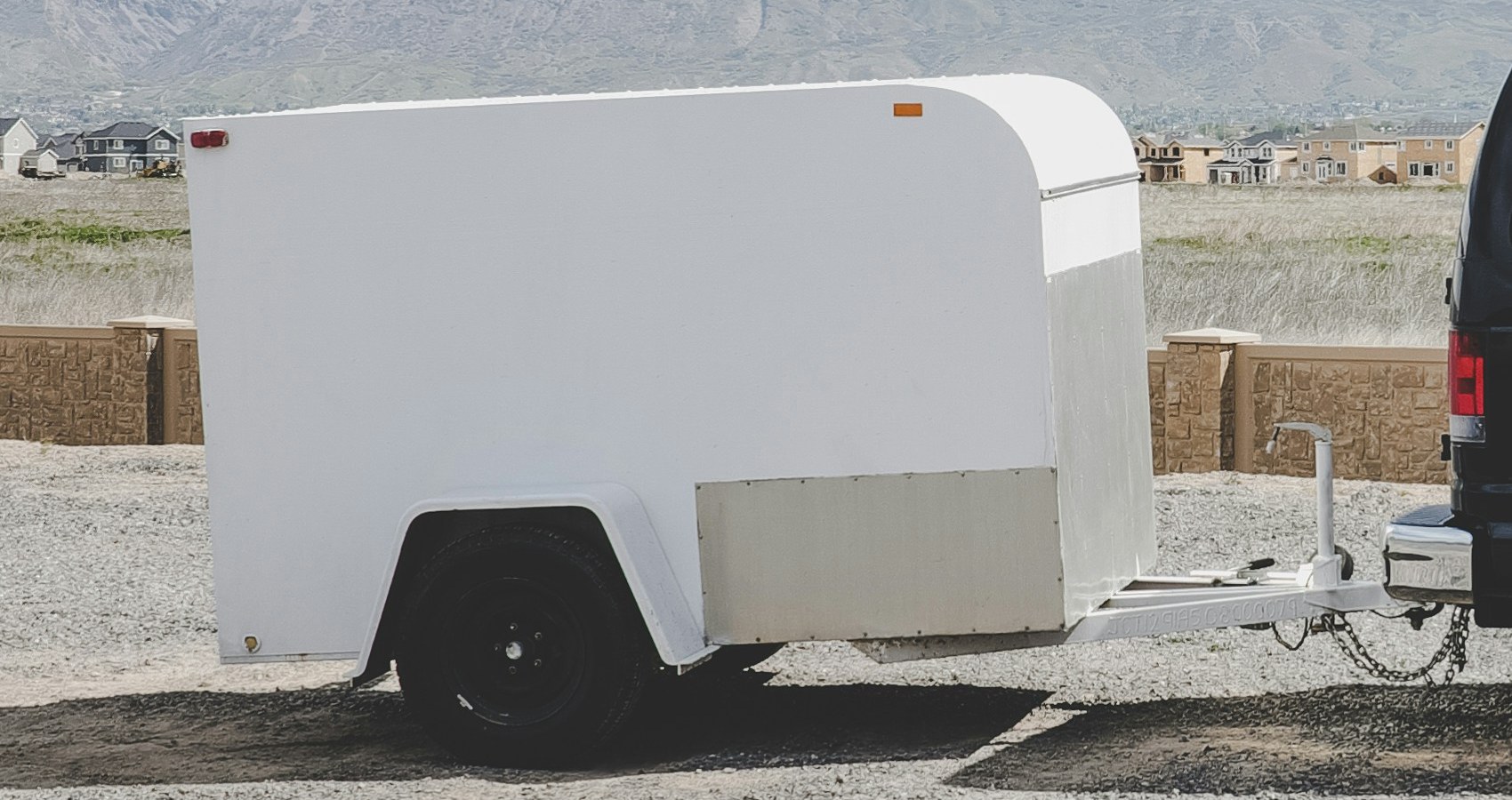 Passenger van towing a small enclosed cargo trailer past snow capped mountains