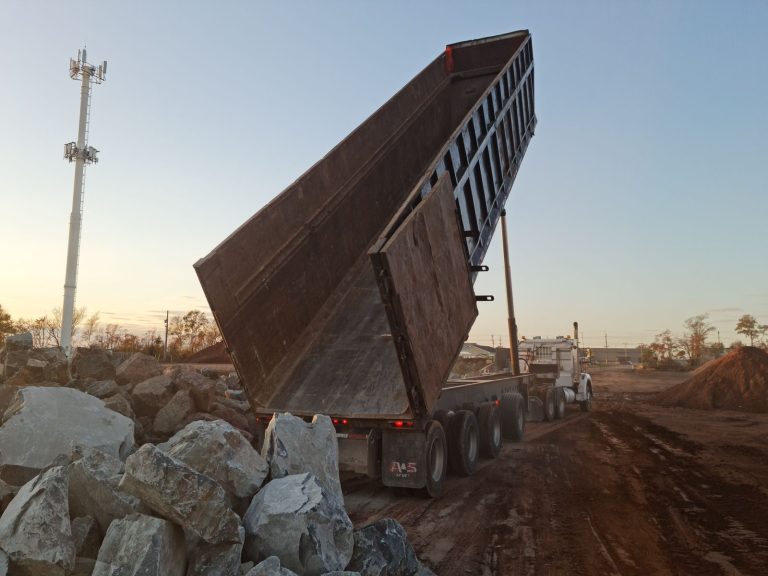 Quad axle end dump trailer raised to unload rock at a job site
