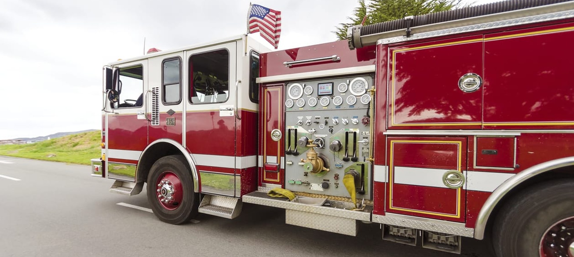 Red and white US fire engine pumper photographed side on with the pump panel and controls visible
