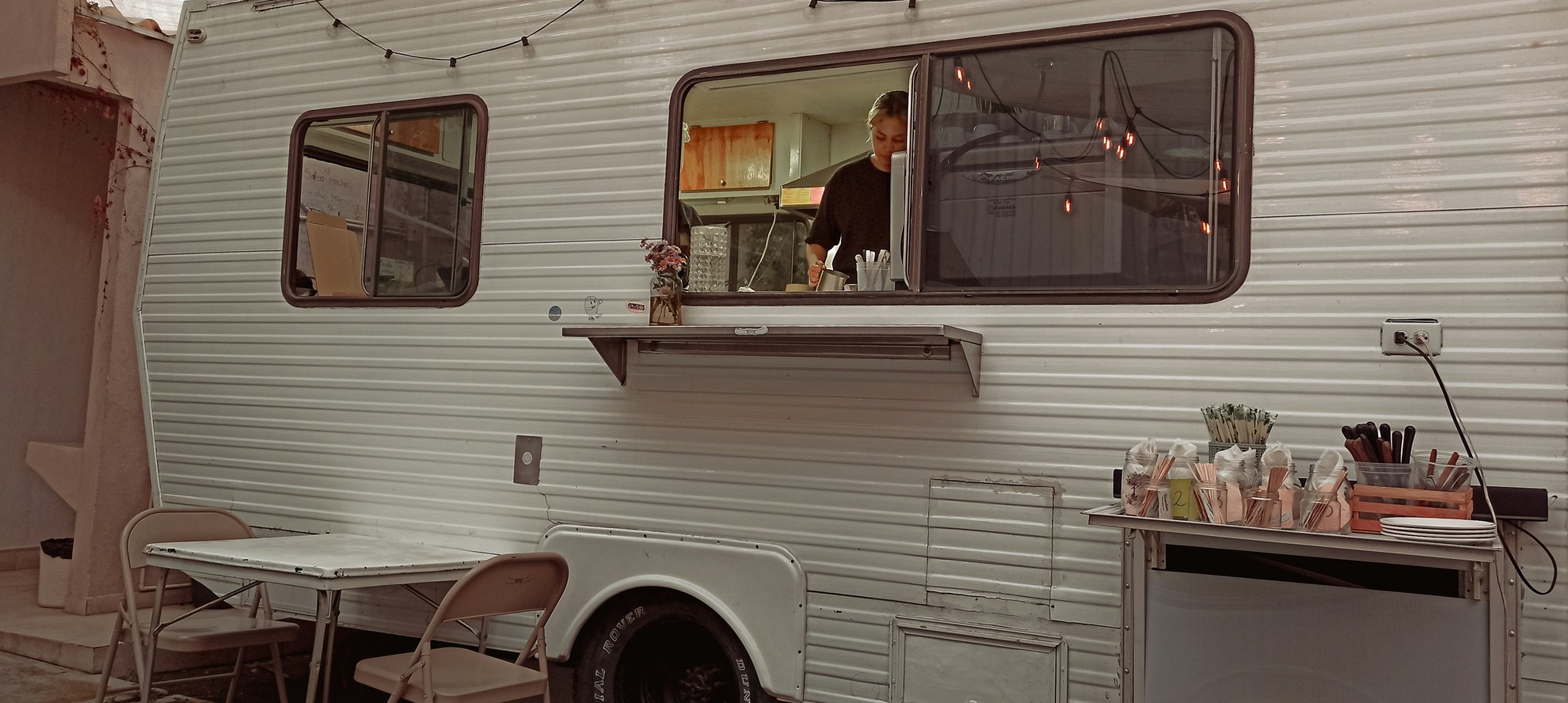 White food trailer with its serving window open and a vendor working inside
