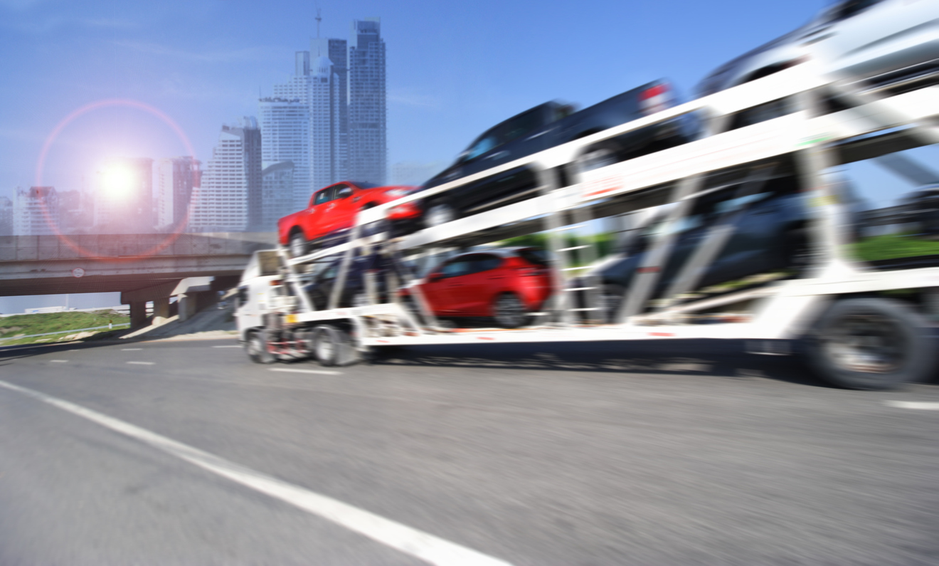 Open car carrier loaded with vehicles passing a city skyline