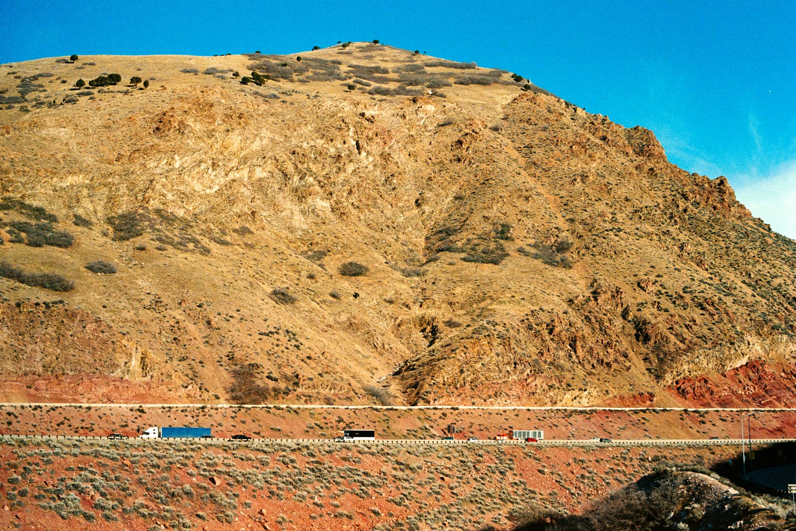Semi trucks running a sunny interstate beneath a dry western mountainside