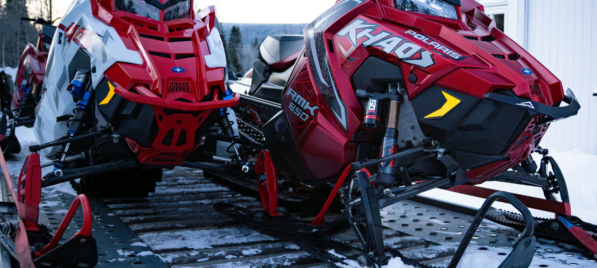 Two Polaris snowmobiles secured with ratchet straps on an open trailer deck in winter