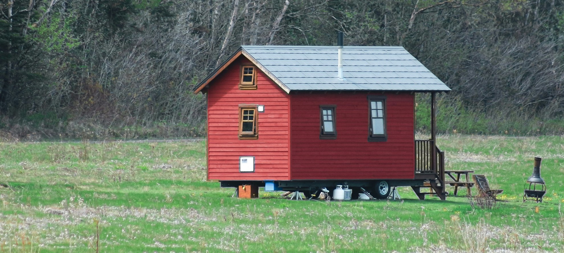 Red tiny house built on a trailer with its wheels and hitch visible