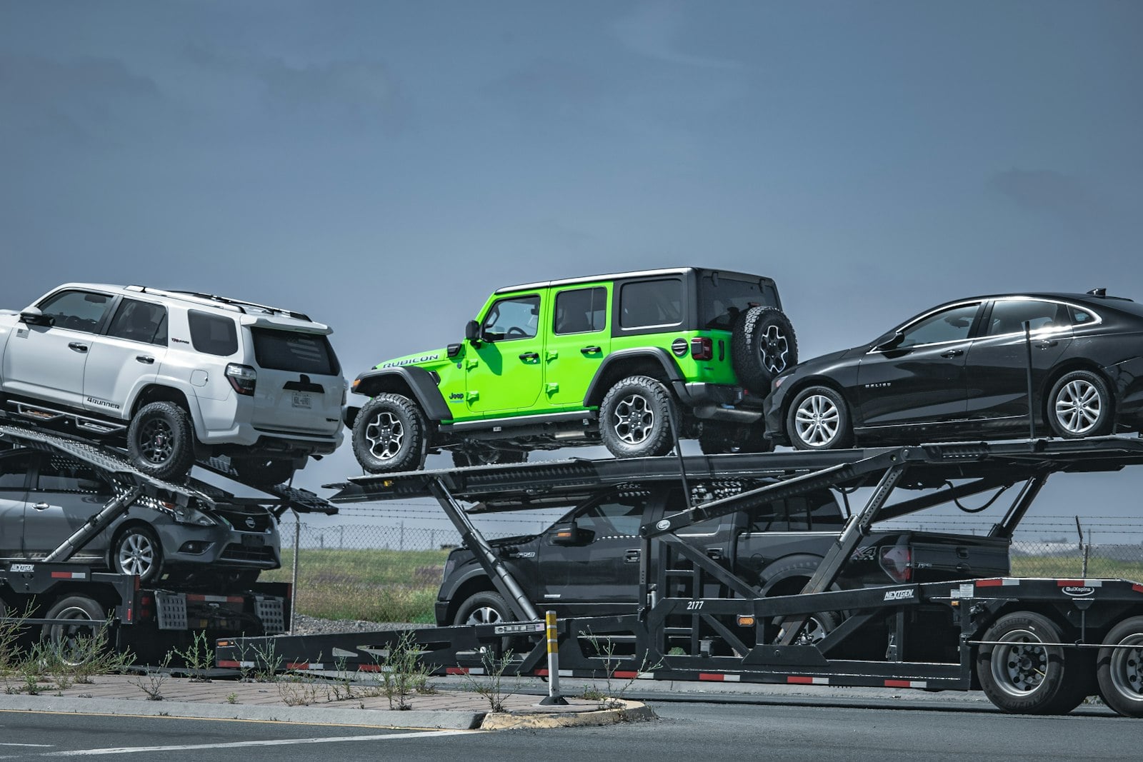 Open auto transport carrier loaded with a Toyota 4Runner, a green Jeep Wrangler and a black sedan